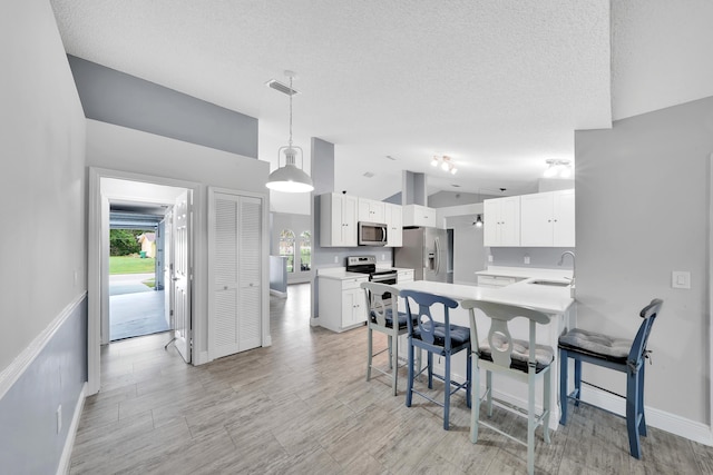 kitchen with white cabinets, sink, a textured ceiling, appliances with stainless steel finishes, and decorative light fixtures