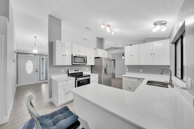 kitchen featuring kitchen peninsula, appliances with stainless steel finishes, vaulted ceiling, sink, and white cabinetry