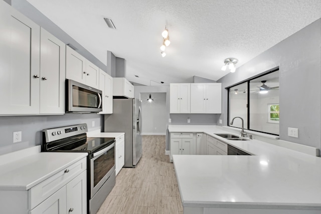 kitchen featuring a textured ceiling, stainless steel appliances, vaulted ceiling, sink, and white cabinets