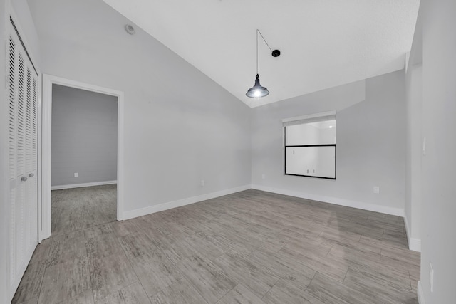 spare room with light wood-type flooring and high vaulted ceiling