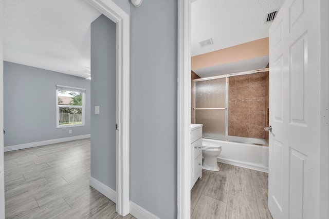 full bathroom with shower / bath combination with glass door, a textured ceiling, vanity, and toilet