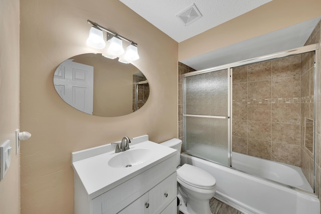 full bathroom featuring shower / bath combination with glass door, vanity, a textured ceiling, and toilet