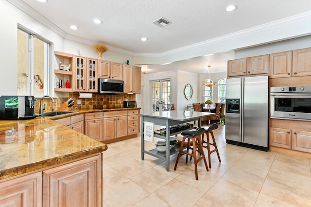 kitchen with appliances with stainless steel finishes, light brown cabinetry, light stone counters, sink, and light tile patterned floors