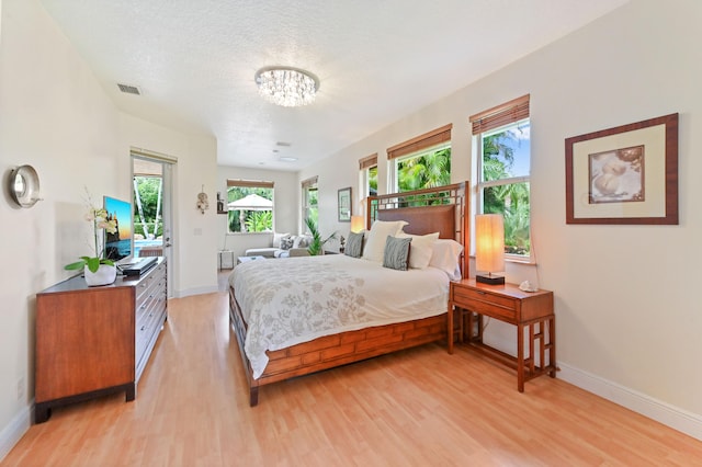 bedroom featuring multiple windows, light hardwood / wood-style flooring, and a textured ceiling