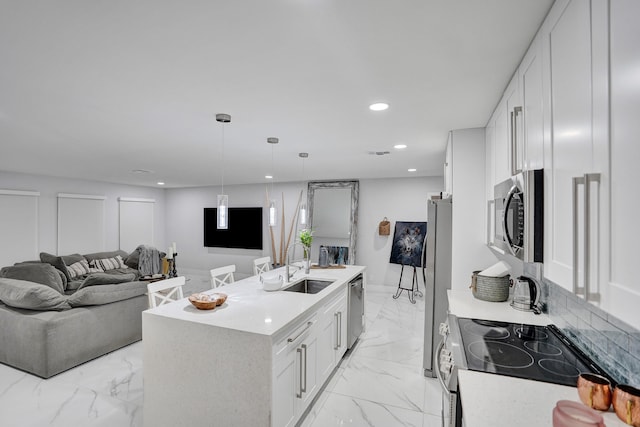 kitchen featuring a kitchen island with sink, hanging light fixtures, sink, appliances with stainless steel finishes, and white cabinetry