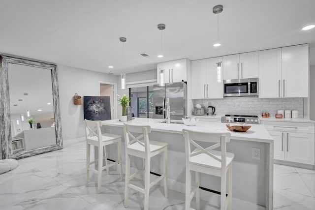 kitchen with appliances with stainless steel finishes, white cabinetry, a kitchen island with sink, and pendant lighting