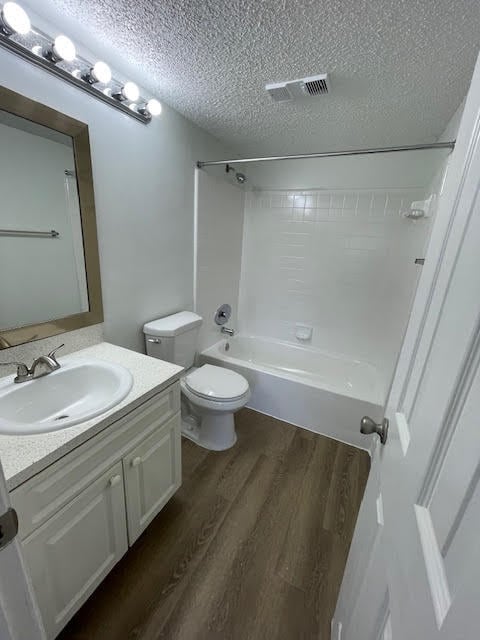 full bathroom featuring vanity, a textured ceiling, hardwood / wood-style flooring, shower / bathing tub combination, and toilet