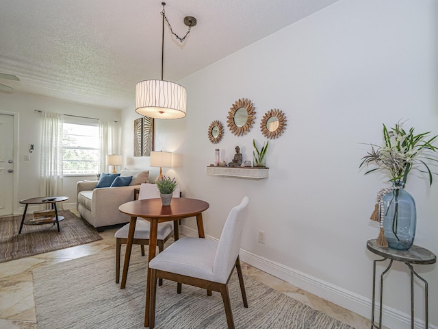 dining space with a textured ceiling, marble finish floor, and baseboards