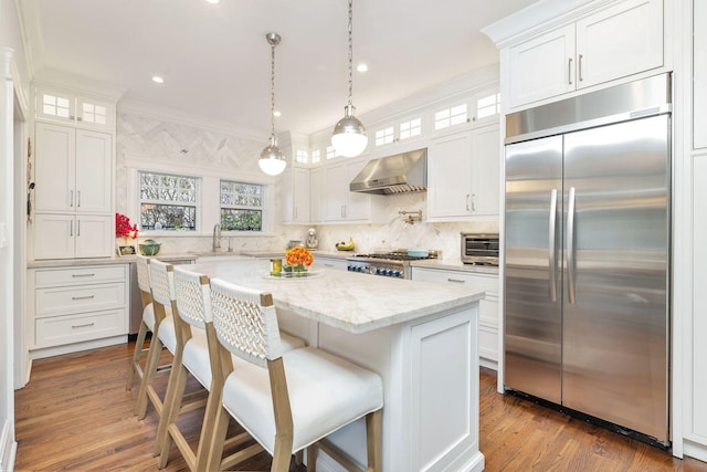 kitchen with appliances with stainless steel finishes, crown molding, white cabinetry, and wall chimney range hood