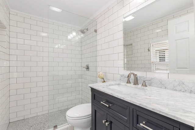 bathroom with vanity, toilet, a tile shower, and tile walls