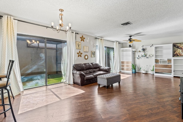 living room featuring dark wood-type flooring, a barn door, ceiling fan with notable chandelier, and a textured ceiling