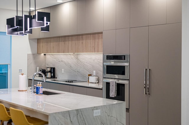 kitchen featuring pendant lighting, sink, stainless steel double oven, light stone countertops, and decorative backsplash