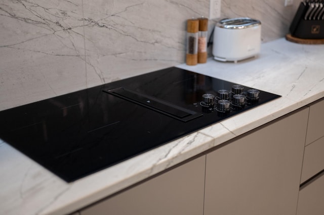 room details with light stone countertops, decorative backsplash, and black electric stovetop