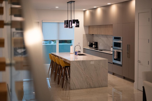 kitchen with an island with sink, stainless steel double oven, sink, decorative light fixtures, and a kitchen breakfast bar