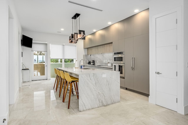 kitchen with light stone counters, an island with sink, hanging light fixtures, sink, and gray cabinets