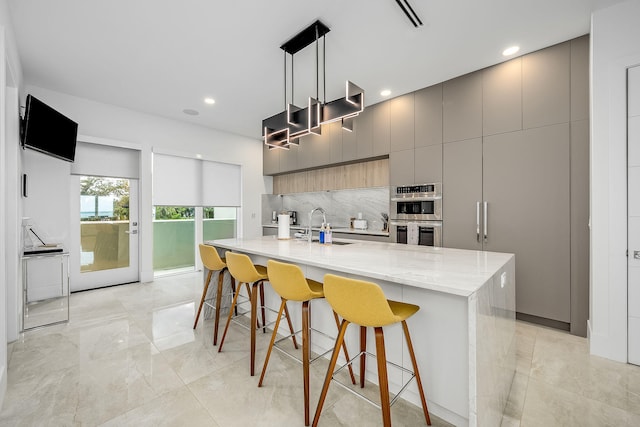 kitchen with gray cabinetry, decorative light fixtures, decorative backsplash, double oven, and a spacious island