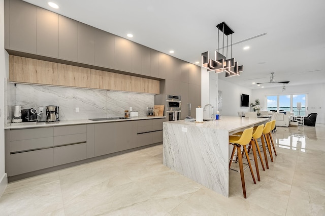 kitchen with pendant lighting, backsplash, gray cabinets, and a large island with sink