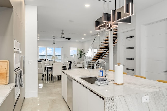 kitchen featuring light stone counters, sink, white cabinetry, decorative light fixtures, and dishwasher