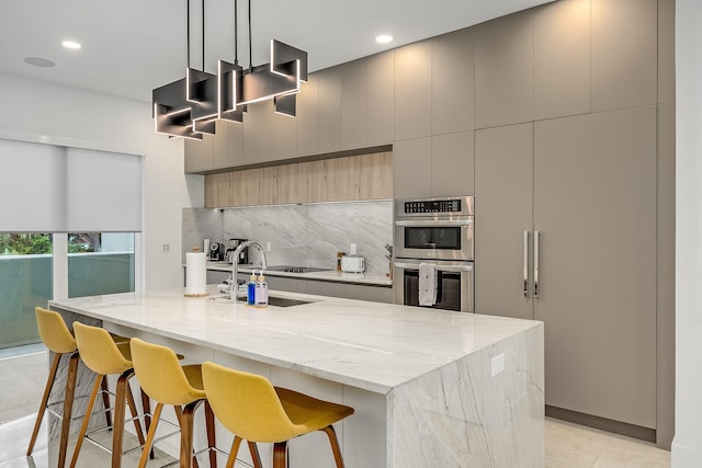 kitchen with stainless steel double oven, light stone countertops, decorative light fixtures, and a large island with sink