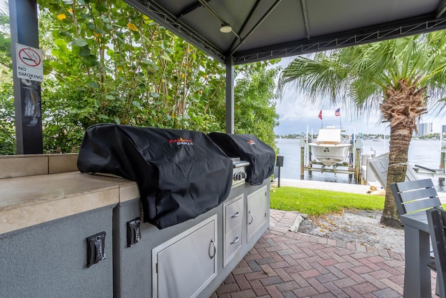 view of patio featuring a boat dock, area for grilling, boat lift, an outdoor kitchen, and a water view