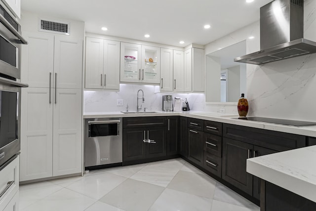 kitchen featuring stainless steel appliances, white cabinets, sink, wall chimney range hood, and backsplash