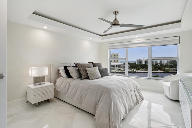 bedroom with a raised ceiling, baseboards, a city view, ceiling fan, and a water view