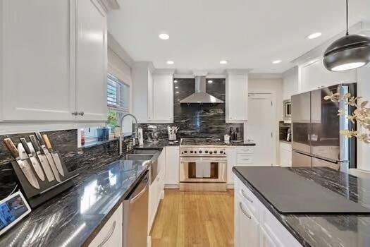 kitchen featuring decorative backsplash, wall chimney exhaust hood, light hardwood / wood-style flooring, premium appliances, and white cabinets