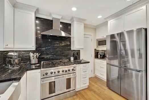 kitchen featuring white cabinets, tasteful backsplash, light hardwood / wood-style floors, wall chimney exhaust hood, and stainless steel appliances