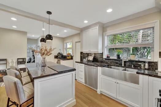 kitchen featuring a kitchen island, white cabinetry, dishwasher, pendant lighting, and sink