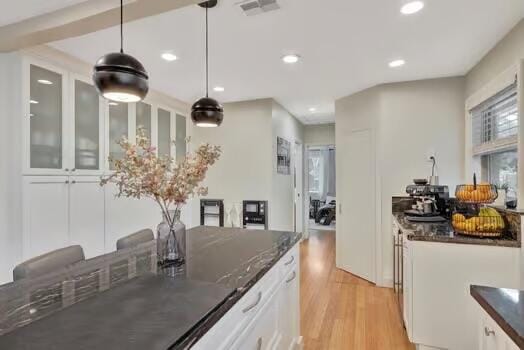 kitchen featuring white cabinets, dark stone counters, light wood-type flooring, and hanging light fixtures