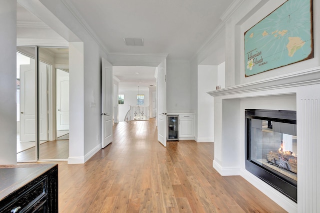 hallway with ornamental molding, beverage cooler, and light hardwood / wood-style floors