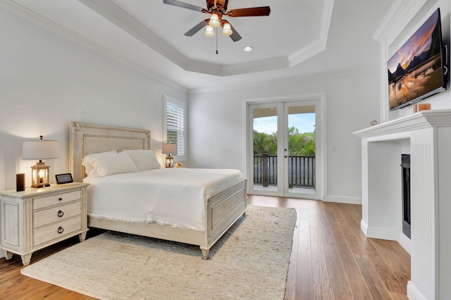 bedroom with access to outside, ceiling fan, ornamental molding, a tray ceiling, and light wood-type flooring