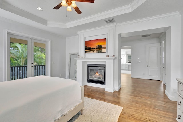 bedroom with light wood-type flooring, ceiling fan, access to exterior, a tray ceiling, and crown molding