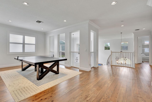 game room with ornamental molding, light wood-type flooring, and a textured ceiling