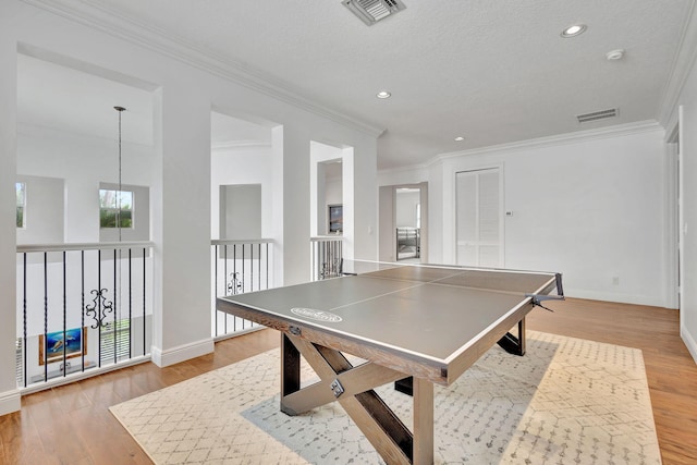 game room featuring ornamental molding, light wood-type flooring, and a textured ceiling