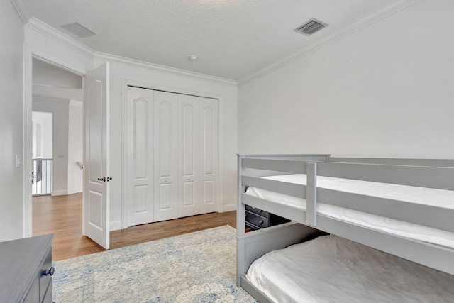 bedroom with a closet, crown molding, hardwood / wood-style flooring, and a textured ceiling