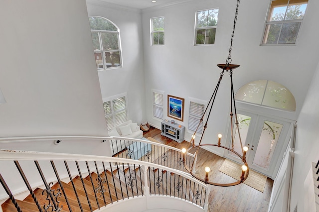 stairway featuring hardwood / wood-style flooring, crown molding, a high ceiling, and a chandelier