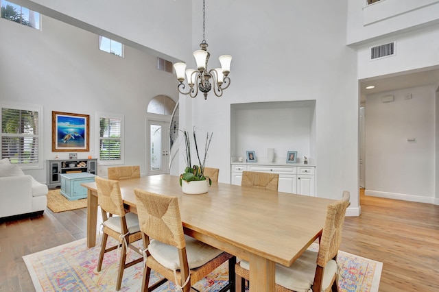 dining area featuring a high ceiling, a healthy amount of sunlight, a chandelier, and light hardwood / wood-style flooring