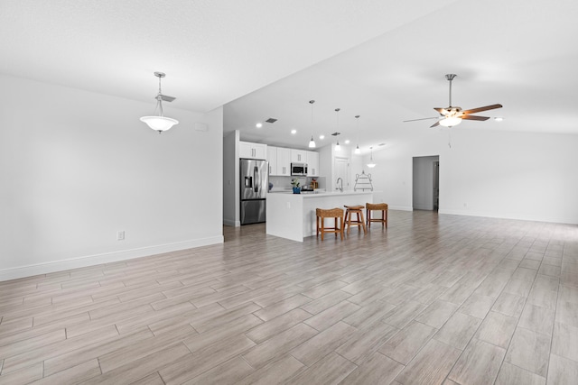 unfurnished living room featuring sink, ceiling fan, vaulted ceiling, and light hardwood / wood-style floors