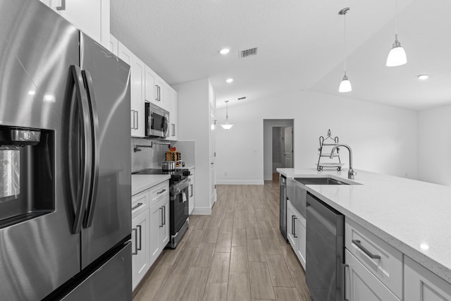 kitchen featuring decorative light fixtures, stainless steel appliances, vaulted ceiling, and white cabinetry