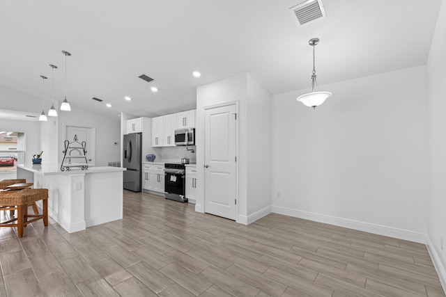 kitchen featuring white cabinets, lofted ceiling, decorative light fixtures, a kitchen breakfast bar, and stainless steel appliances