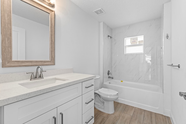 full bathroom with a textured ceiling, tiled shower / bath combo, vanity, and toilet