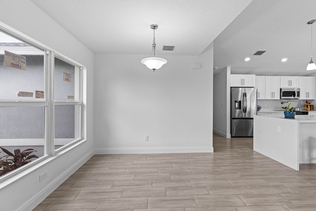 interior space featuring light hardwood / wood-style floors, stainless steel appliances, hanging light fixtures, white cabinets, and a textured ceiling