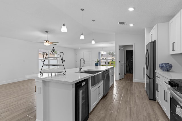 kitchen featuring beverage cooler, a kitchen island with sink, vaulted ceiling, and white cabinetry