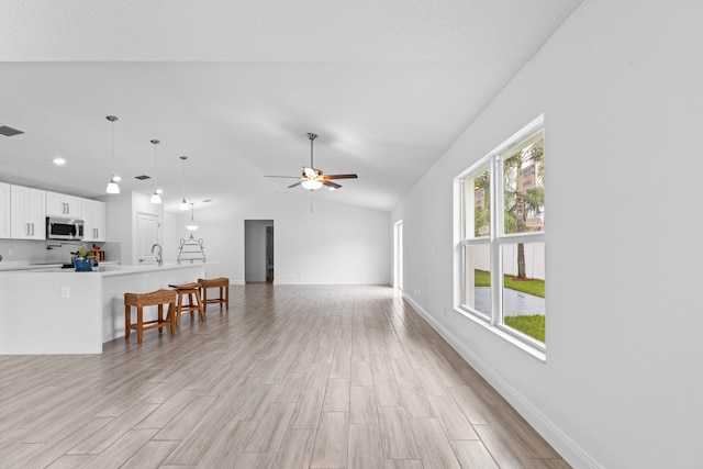 living room with ceiling fan, lofted ceiling, light wood-type flooring, and sink