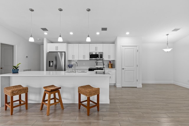 kitchen featuring hanging light fixtures, sink, white cabinetry, appliances with stainless steel finishes, and a breakfast bar area