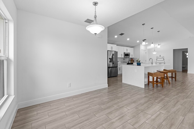 kitchen featuring stainless steel appliances, pendant lighting, white cabinets, and a center island with sink