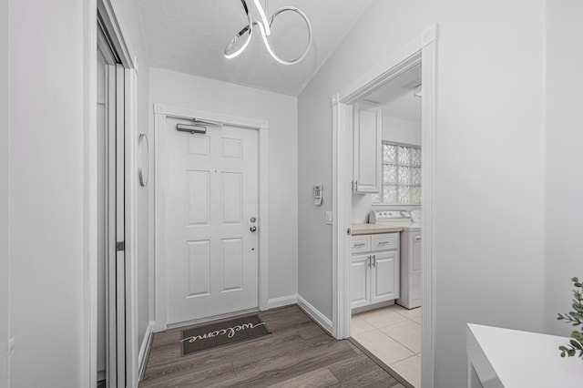 doorway with washer / dryer, a textured ceiling, and light wood-type flooring