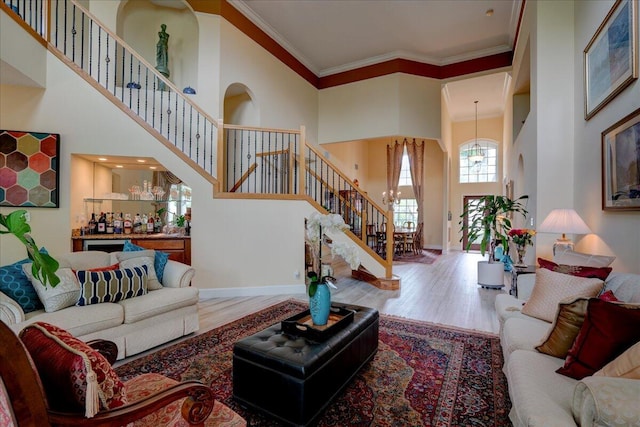 living room with indoor bar, hardwood / wood-style flooring, a high ceiling, a notable chandelier, and crown molding