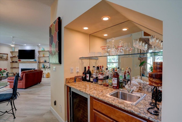 bar featuring beverage cooler, light stone countertops, sink, and light hardwood / wood-style flooring